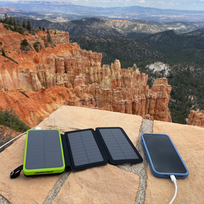 JackPak PB20KS solar power bank with foldable solar panels charging a phone, set on a stone with a scenic mountain view in the background.