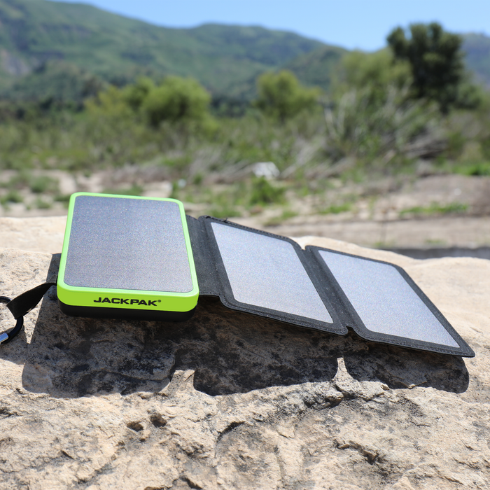 JackPak PB20KS solar power bank with foldable solar panels, placed on a rock in the outdoors, charging under the sun.